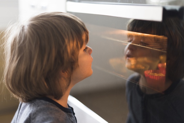 Na zdjęciu znajduje się dziecko, które spogląda przez szybę do wnętrza piekarnika.
